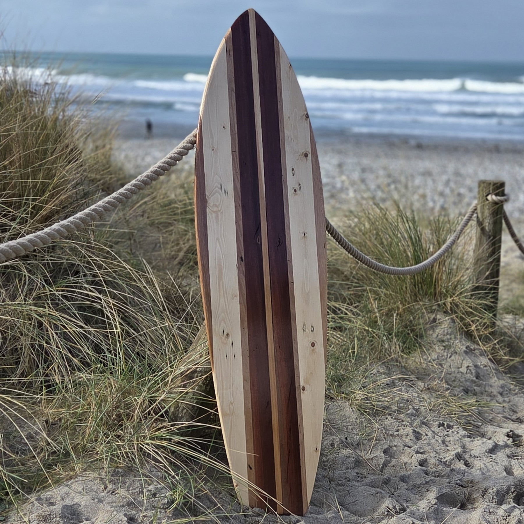 Wooden surfboard leaning against a fence on a sandy beach with ocean waves in the background